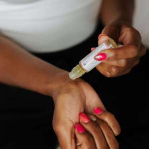 Close-up of a woman applying perfume oil on her wrist, showcasing nail art and skin care.