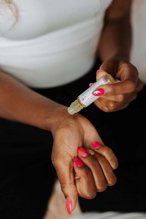 Close-up of a woman applying perfume oil on her wrist, showcasing nail art and skin care.