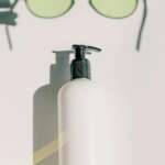 Chic aesthetic featuring a skincare bottle and eyeglasses on a white background.
