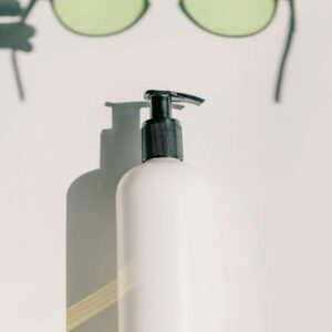 Chic aesthetic featuring a skincare bottle and eyeglasses on a white background.