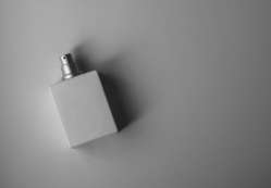 A sleek white perfume bottle photographed on a gray background with soft, muted lighting.
