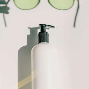 Chic aesthetic featuring a skincare bottle and eyeglasses on a white background.