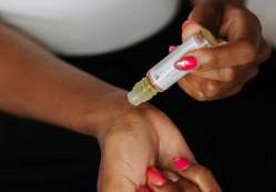 Close-up of a woman applying perfume oil on her wrist, showcasing nail art and skin care.